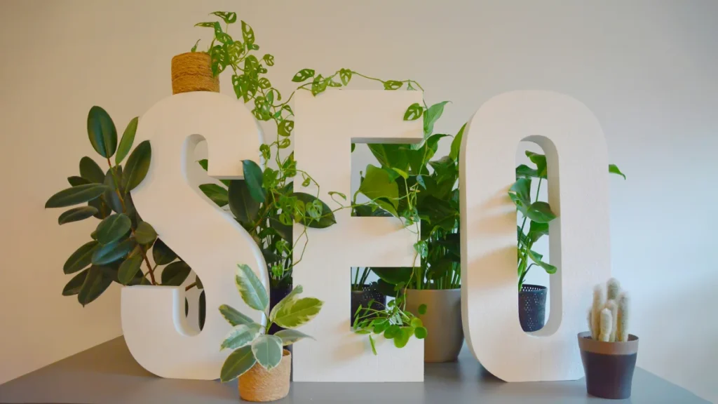 the text seo is shown with a couple of white wooden blocks, surrounded by plants, placed on a table